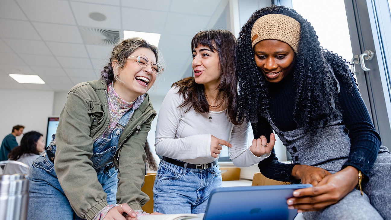 Two or three students are standing around a seminar table, looking at a tablet together.