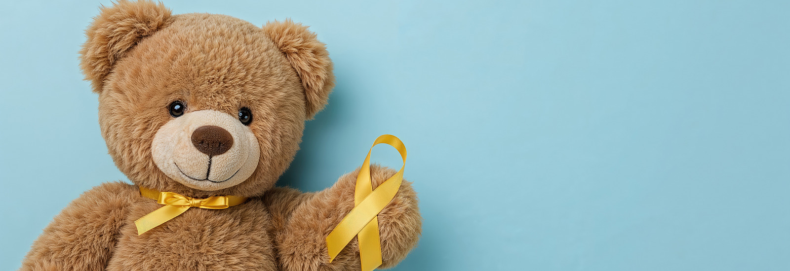 A fabric teddy bear holds up a yellow bow