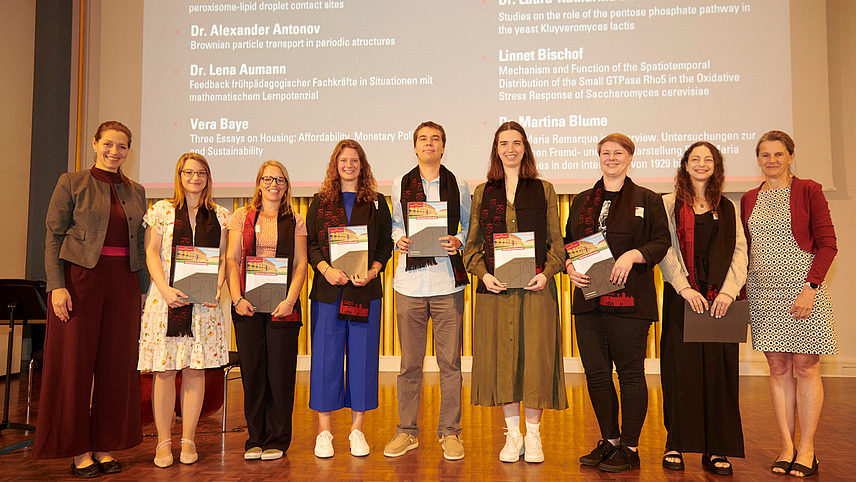 Several people stand on a stage, holding certificates in their hands and smiling into the camera