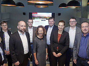 8 Personen haben sich für ein Foto vor einem interaktiven Whiteboard aufgestellt.