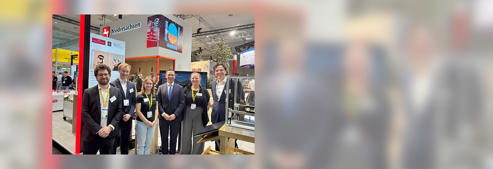 A group of men and women are standing between exhibition booths a smile into the camera