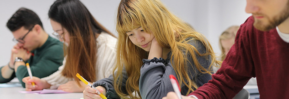 Four students sitting at a table, looking concentrated and writing