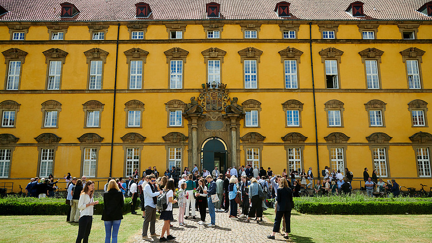 Numerous people stand in front of a historic building.