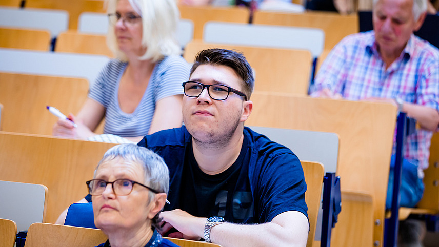View of students across the rows of seats in a lecture hall, among them three elderly people.