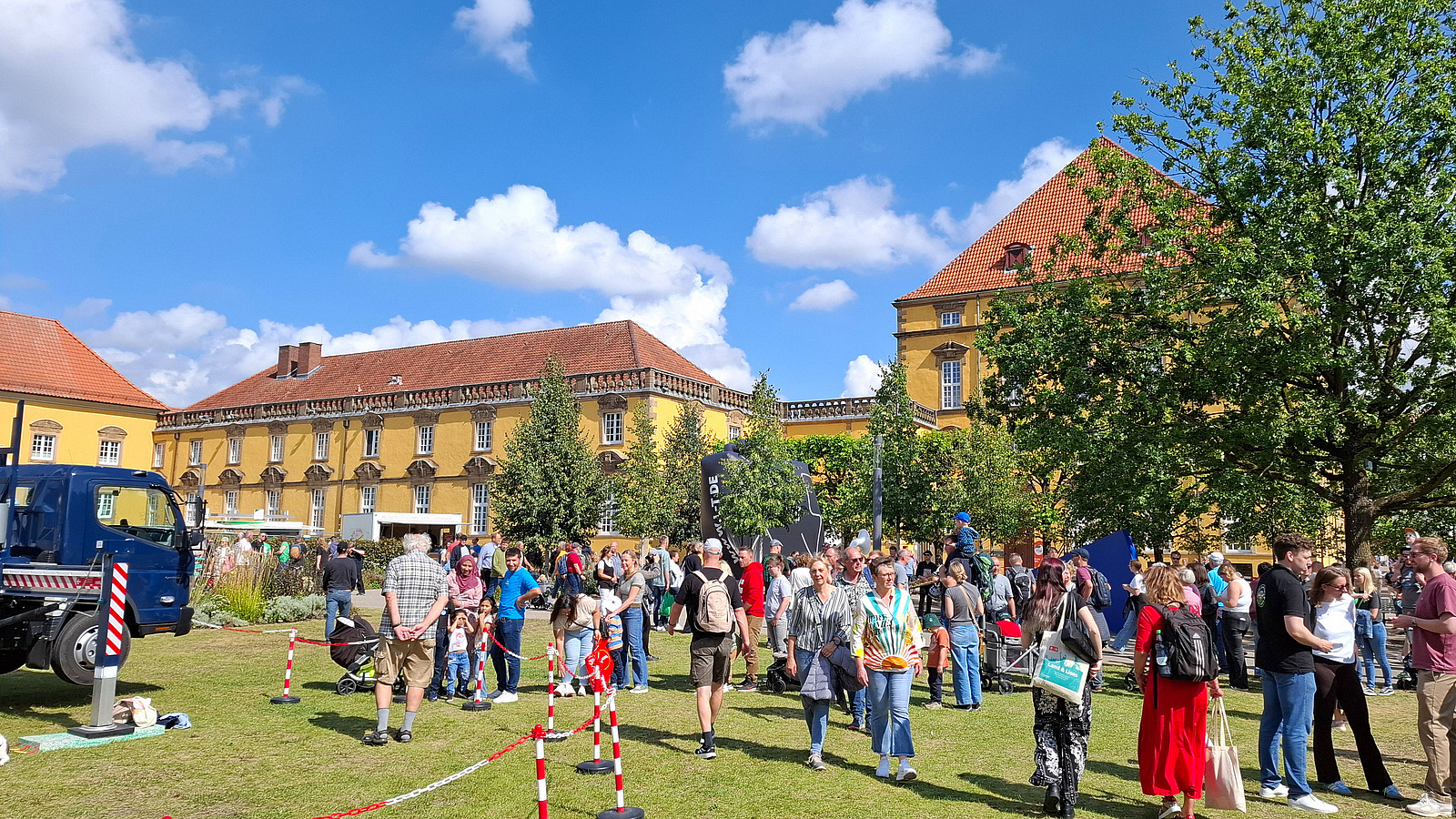 Crowd in front of a historic building with trees and a truck in the foreground.
