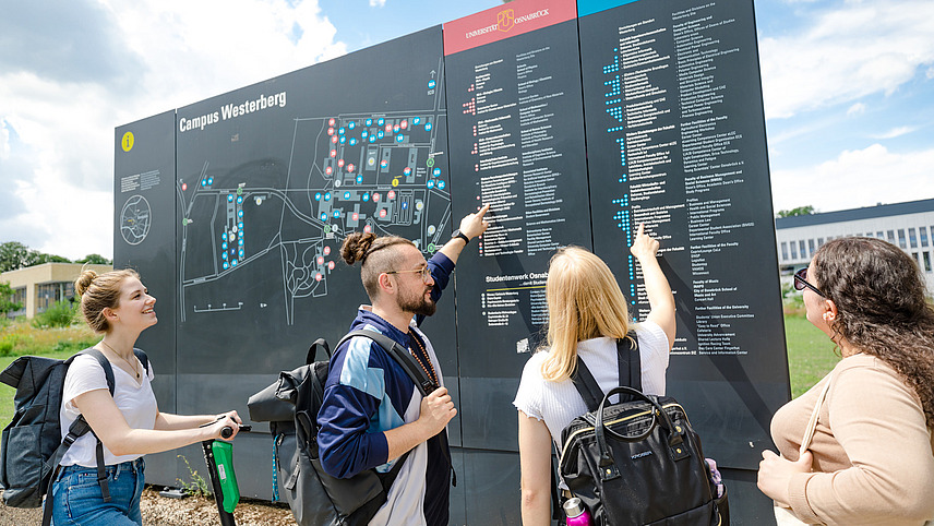 A few students point their fingers at buildings on a large map of Westerberg 