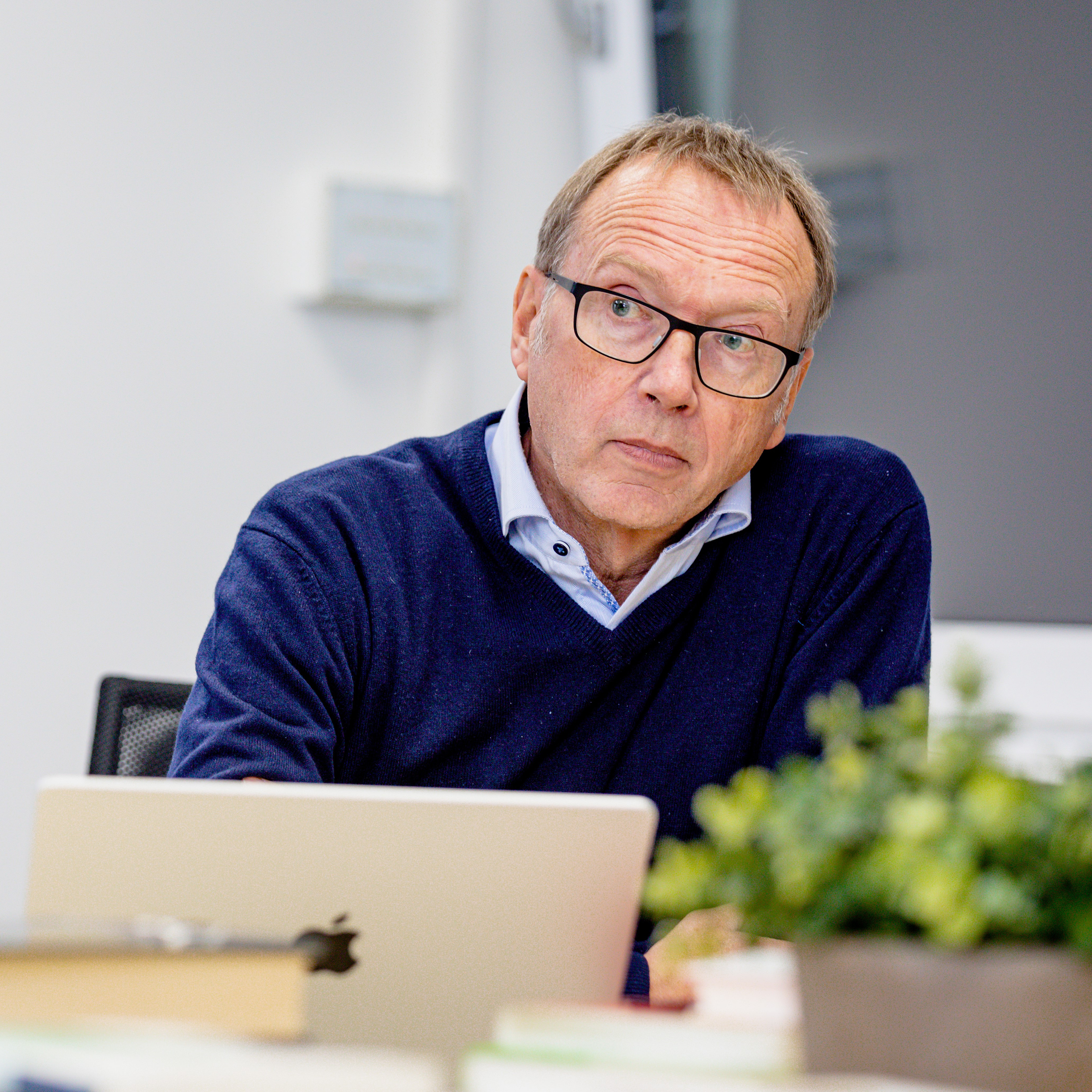Das Bild zeigt Achim Stephan frontal an einem Tisch. Er sitz in einer Diskussionsrunde und hört mit kritisch-interessiertem Blick zu.