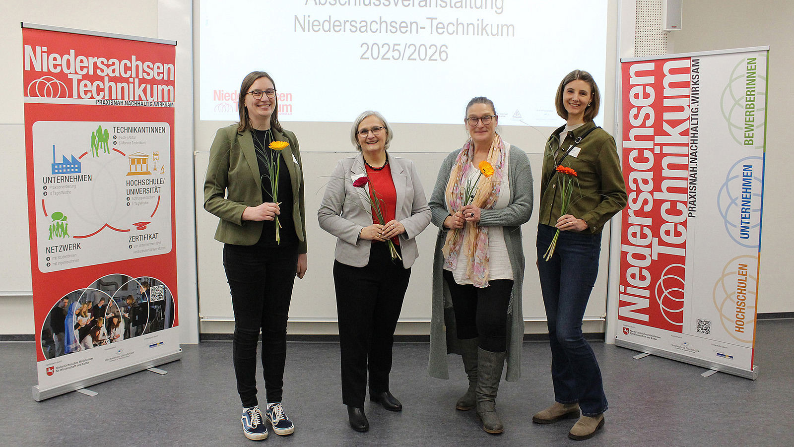 Vier Personen stehen vor Bannern des Nieders&auml;chsischen Technikums und posieren f&uuml;r ein Foto.