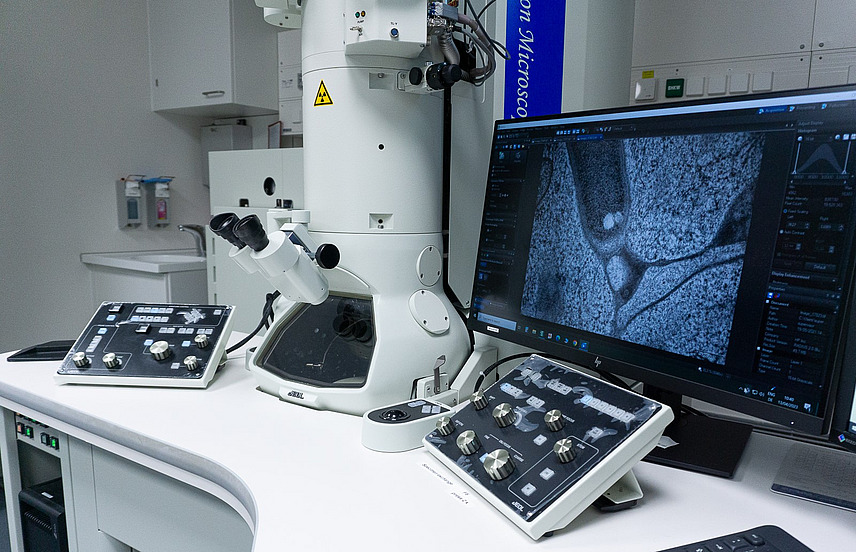A laboratory table with a large microscope, microsocopies can be seen on a screen.