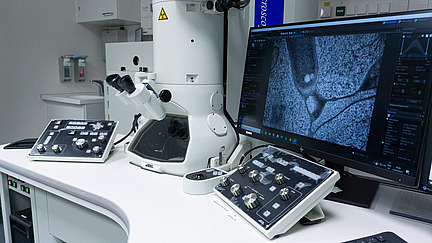 A laboratory table with a large microscope, microsocopies can be seen on a screen.
