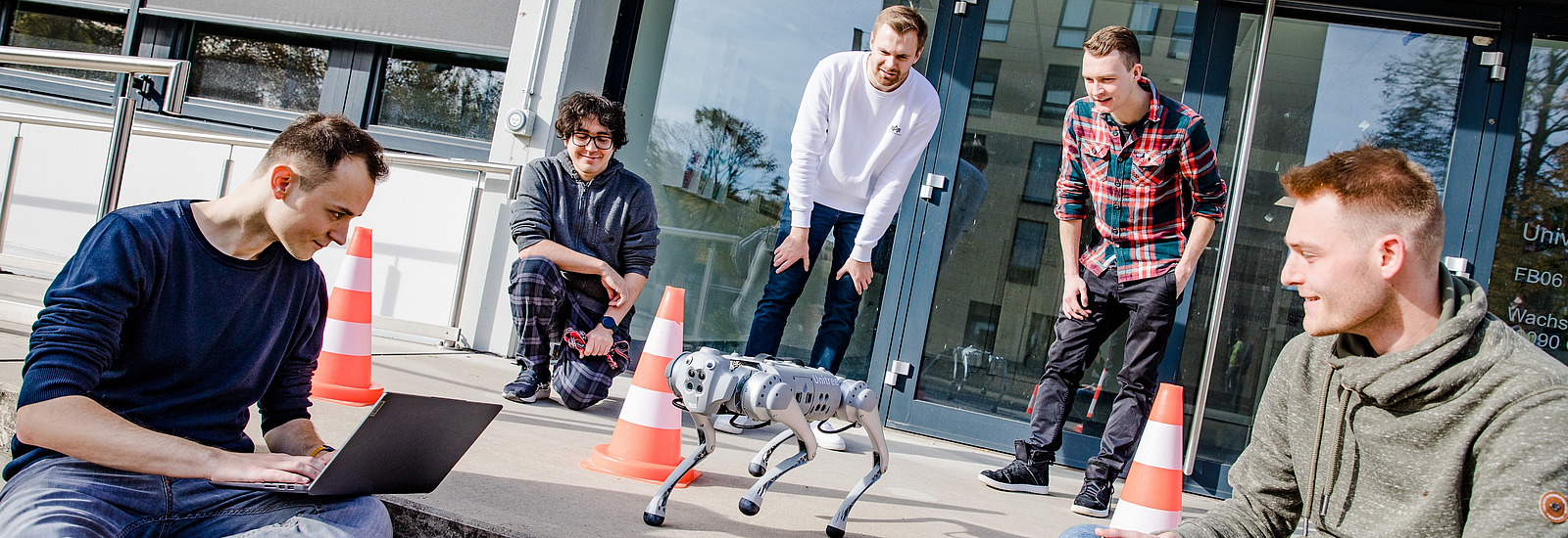 Studierende mit einem Roboterhund auf der Eingangstreppe vor dem Informatik-Gebäude