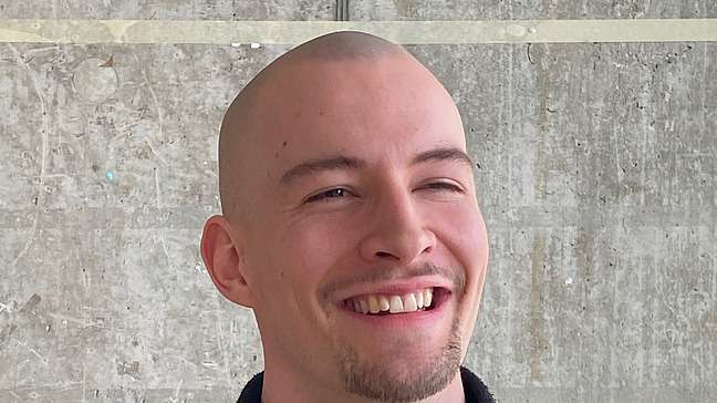 ein junger mann mit rasiertem Kopf lacht in die Kamera