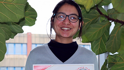 A woman holds a certificate and smiles at the camera