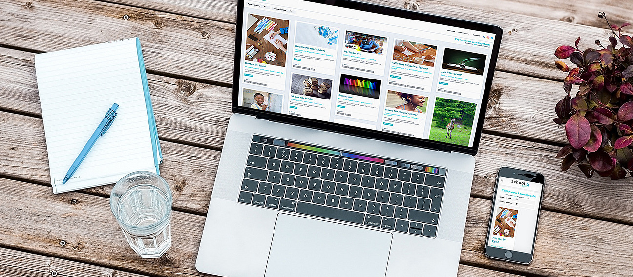 Folgende Sachen liegen auf einem hölzernen Tisch: ein Terminkalender mit Stift und Wasserglas, ein Laptop und ein Smartphone