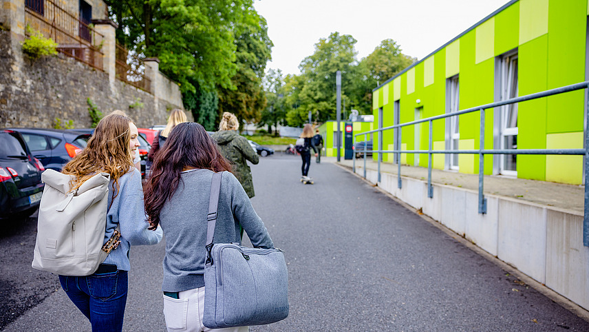 Zwei Studierende laufen zu einem gr&uuml;nen Geb&auml;ude 