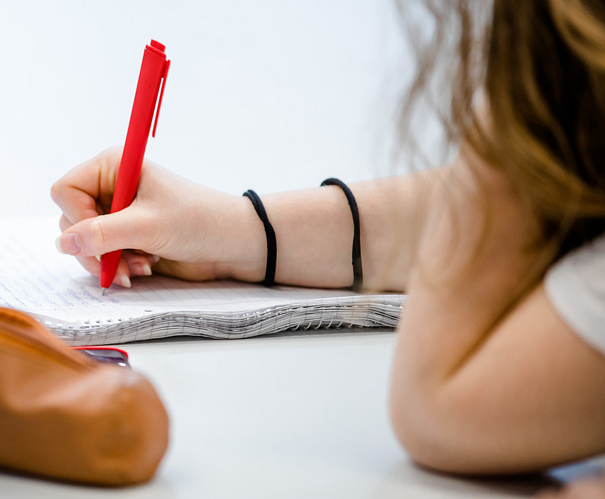 Nahaufnahme eines Blocks, auf dem sich eine Studentin mit einem roten Stift Notizen macht.