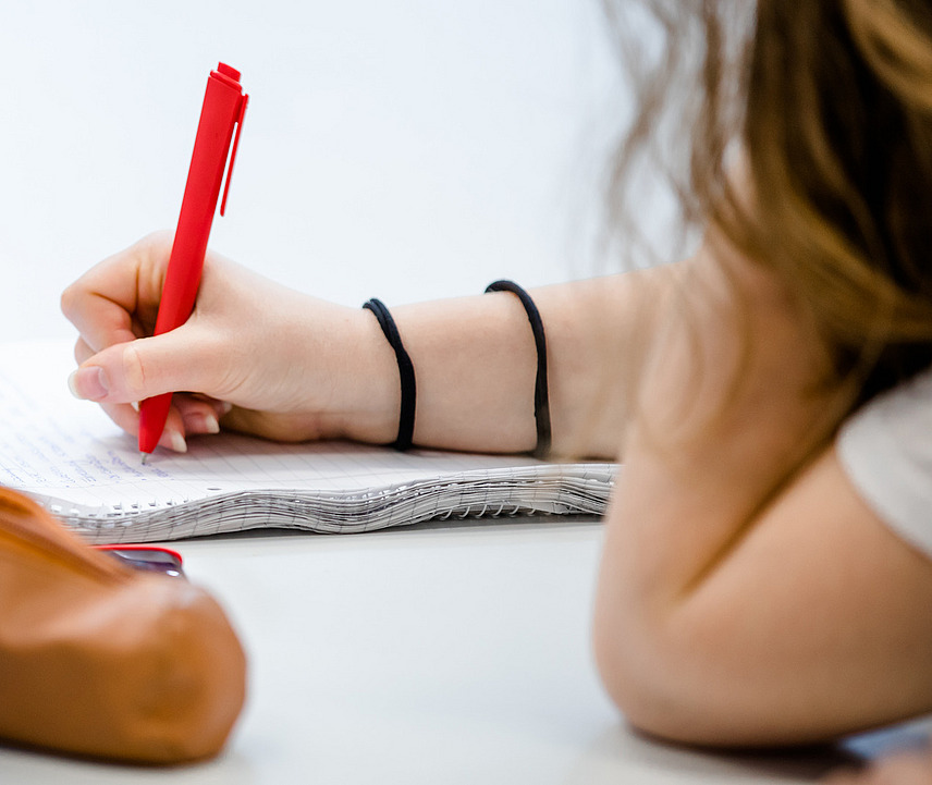 Nahaufnahme eines Blocks, auf dem sich eine Studentin mit einem roten Stift Notizen macht.