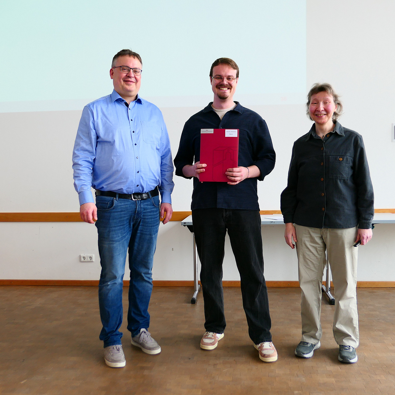 Ein Student steht mit seinem Abschlusszeugnis zwischen Dekan und Studiendekanin.