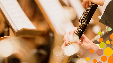 Close-up of a clarinet being played. Other instruments and music stands can be seen blurred in the background.