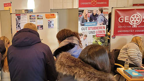 Schülerinnen und Schüler stehen gedrängt, im Hintergrund sind Poster und Infomaterial mit dem Logo der Universität Osnabrück zu sehen.