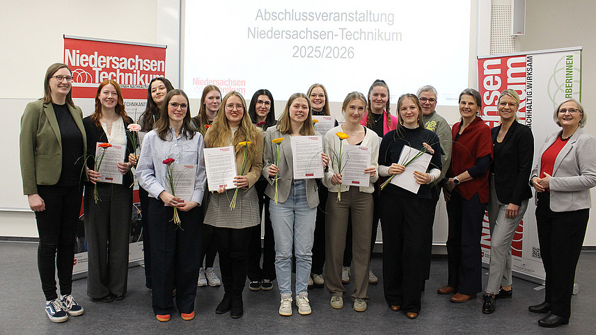 Eine Gruppe von Menschen steht l&auml;chelnd f&uuml;r ein Foto zusammen.