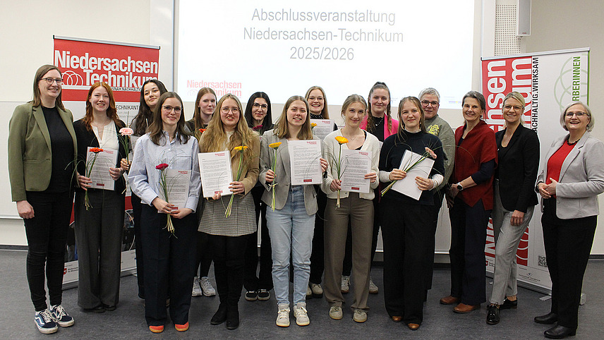 Eine Gruppe von Menschen steht l&auml;chelnd f&uuml;r ein Foto zusammen.