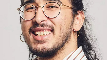 junger Mann mit Brille und dunklen Haaren lächelt freundlich in die Kamera