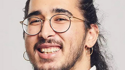 junger Mann mit Brille und dunklen Haaren lächelt freundlich in die Kamera