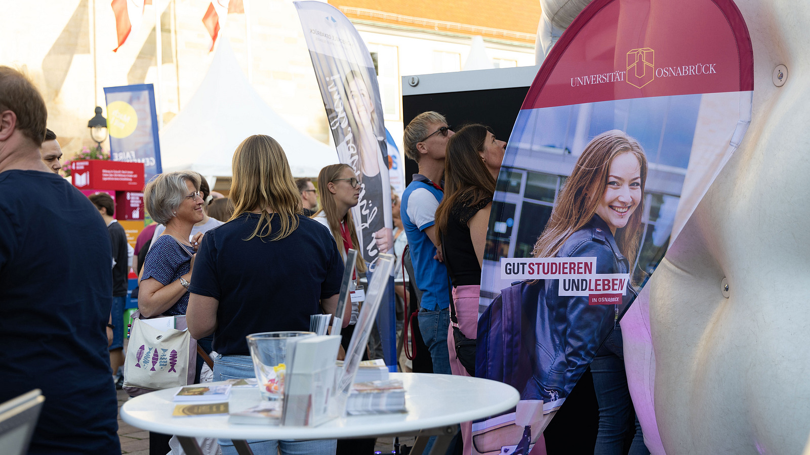 People stand at an information stand with the slogan “Study and live well in Osnabrück.”