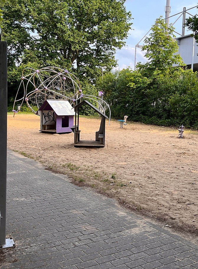 Spielplatz mit rundem Klettergr&uuml;st aus Metall, Wippen und kleinen H&auml;uschen