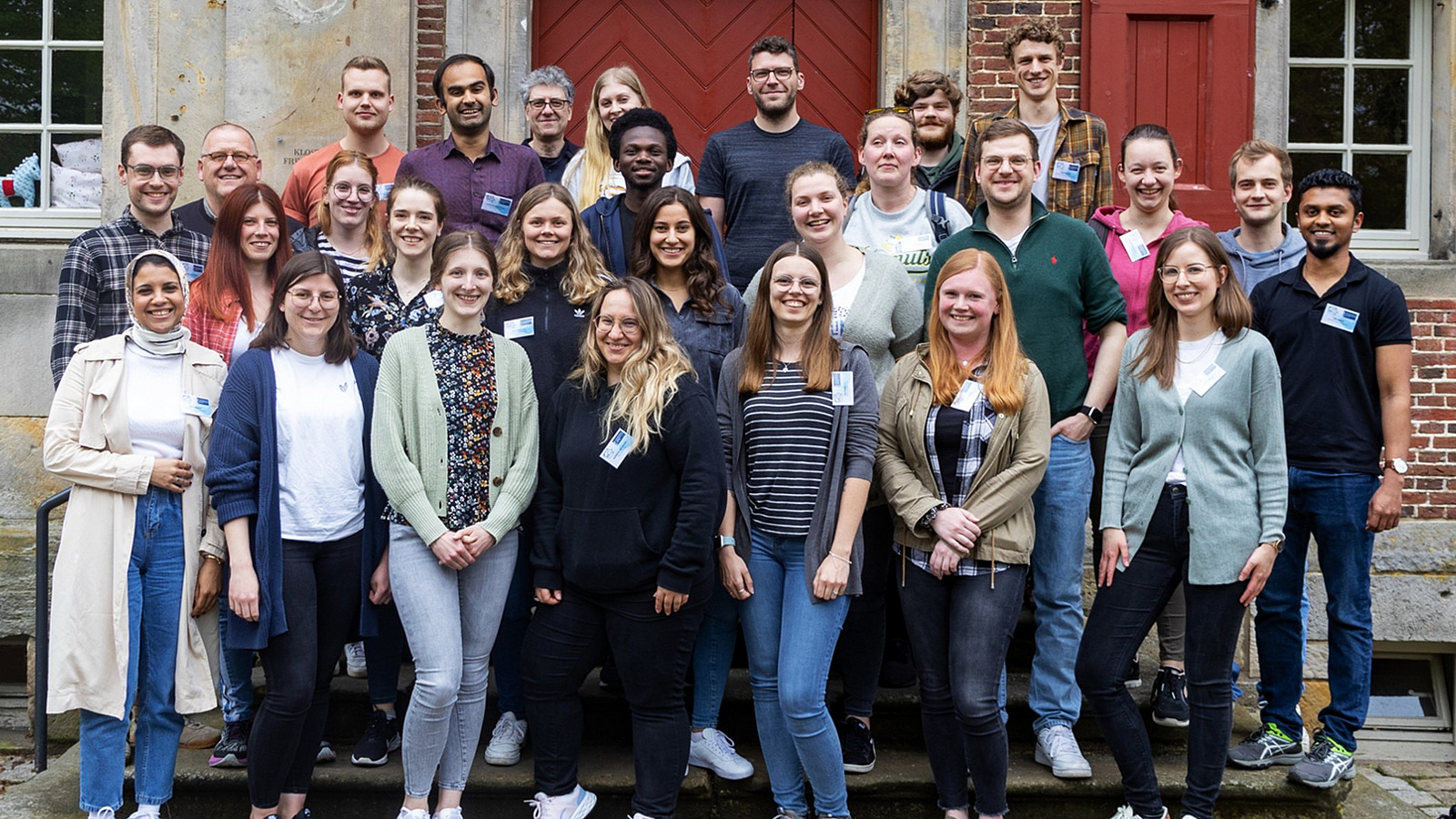 A group of nearly 30 smiling people standing in front of a building