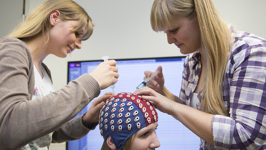 Two female students carry out electroencephalography (EEG) in a laboratory on a third female student to investigate body perception processes.