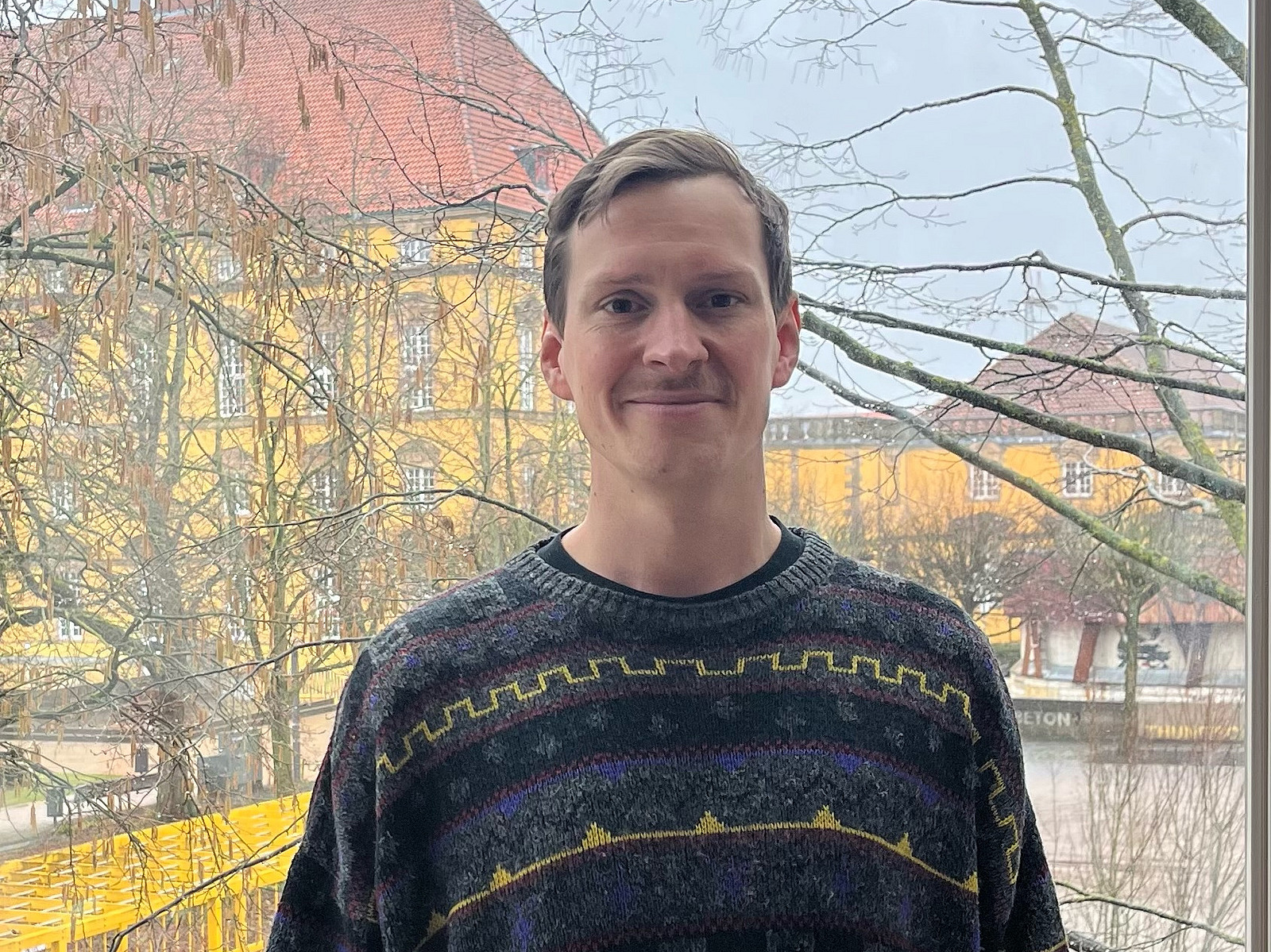 Dr. Benjamin B&uuml;scher steht in einem Pullover vor dem Schloss der Universit&auml;t Osnabr&uuml;ck.