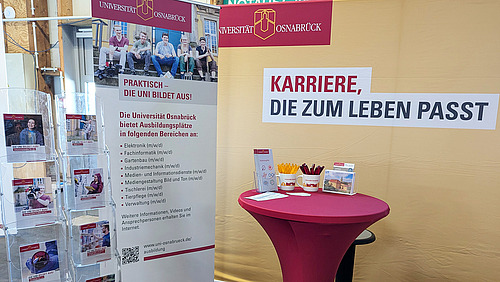 Stand der Universität Osnabrück auf einer Messe, der über Ausbildungsmöglichkeiten informiert. Im Fokus stehen Karrieremöglichkeiten, die zum Leben passen, und verschiedene Ausbildungsbereiche werden vorgestellt.