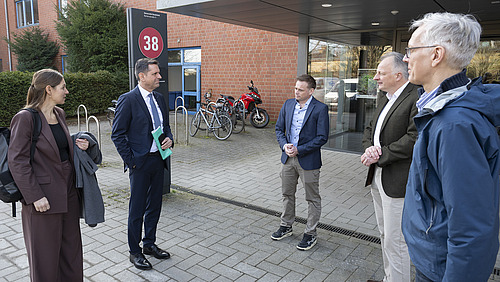 Vier M&auml;nner und eine Frau stehen vor dem Eingang des CellNanOs, auf einem Schild ist in einem roten Kreis die Geb&auml;udenummer &bdquo;38&ldquo; zu erkennen.
