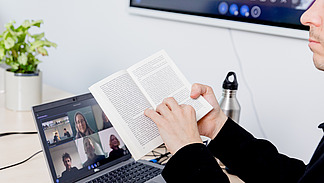 The picture shows the hands of people involved in a discussion during a meeting, for example, with documents and materials spread out on a table in front of them. One person is holding a pen and possibly taking notes.