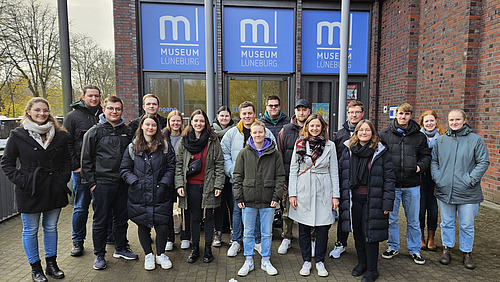 Das Bild zeigt eine Gruppe von Menschen, die warm eingepackt vor dem Eingang des Museums Lüneburg stehen und lächeln.