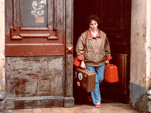 A woman with two suitcases walks through a door. 