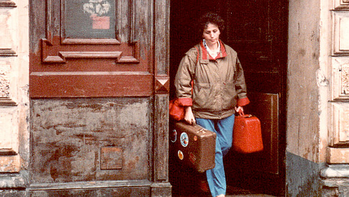 A woman with two suitcases walks through a door. 