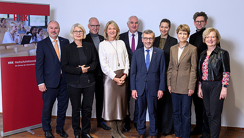 Eine Gruppe formell gejkleideter Personen steht neben einem Aufsteller der Hochschulrektorenkonferenz. Ale lächeln in die Kamera.