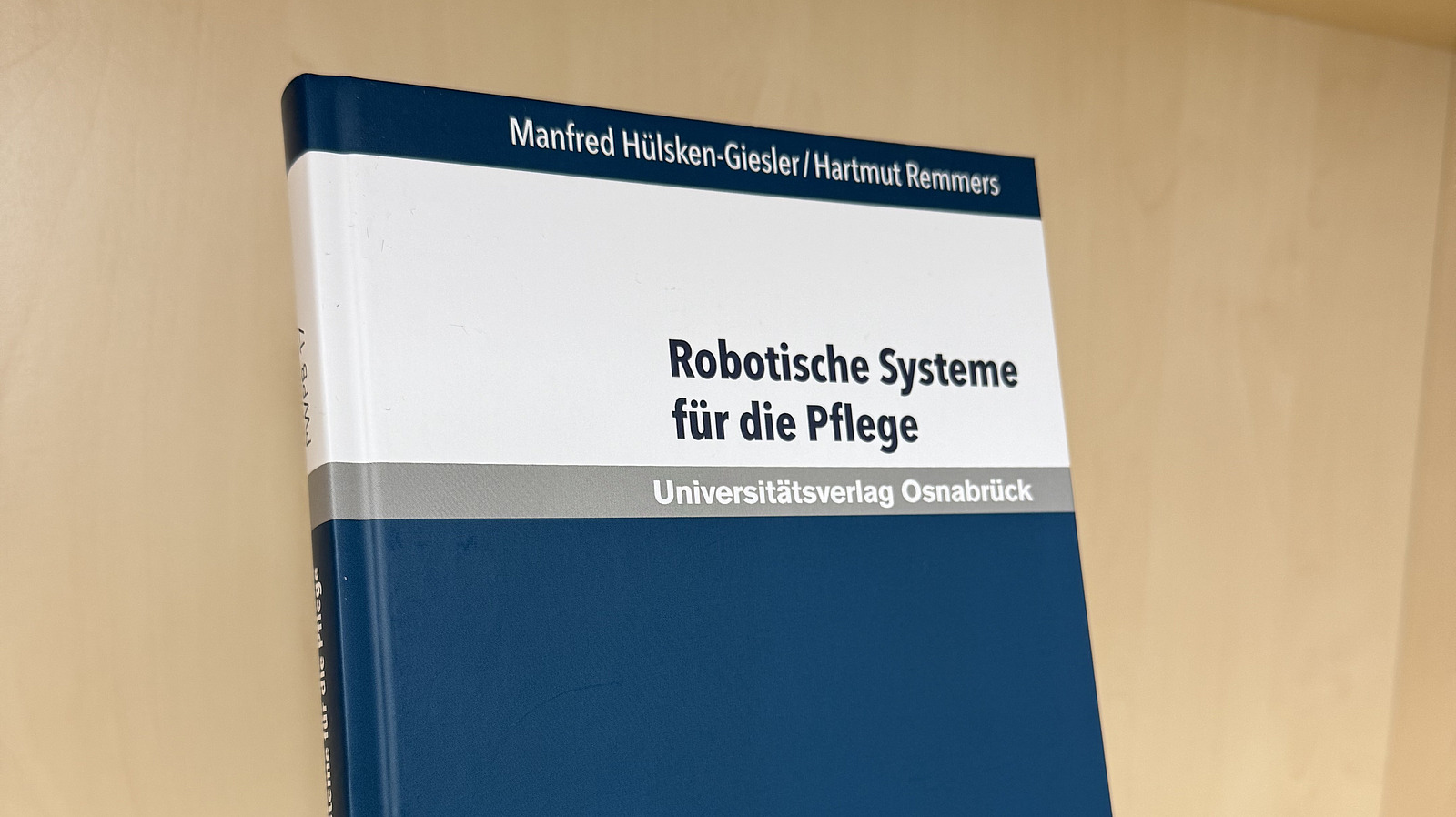 Ein Fachbuch von Manfred H&uuml;lsken-Giesler und Hartmut Remmers mit dem Titel "Robotische Systeme f&uuml;r die Pflege" steht in einem Regal.
