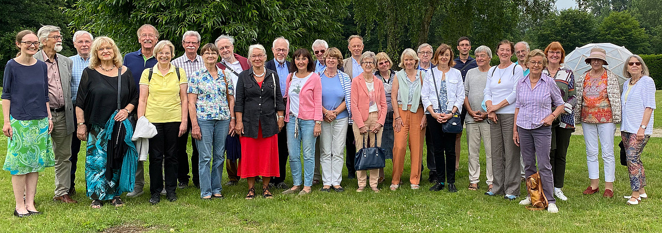 Gruppe von Erwachsenen in Freizeitkleidung posiert auf einer Wiese vor B&uuml;schen und B&auml;umen im Freien