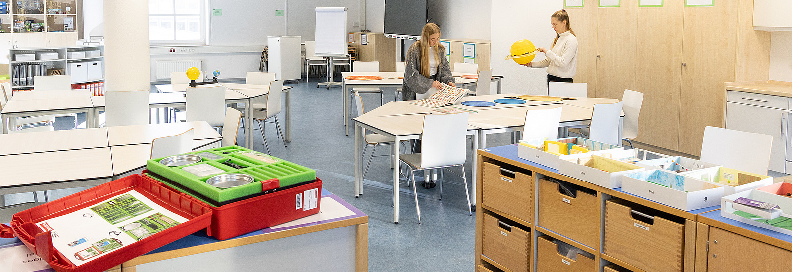 Zwei Studentinnen sitzen an einem Tisch in einer Lernwerkstatt und arbeiten mit Material zum geographischen Lernen.