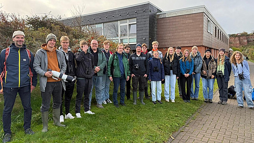 Rund zwanzig Personen stehen vor einem Gebäude, einige tragen Ferngläser.