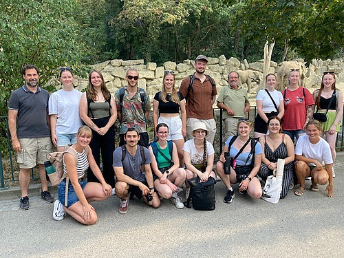 A group of people in front of an elephant enclosure smiling into the camera.