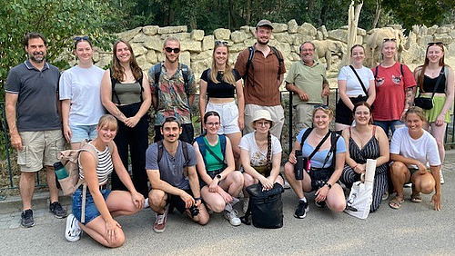 A group of people in front of an elephant enclosure smiling into the camera.