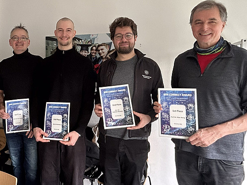 Four men stand side by side, holding certificates in their hands. 