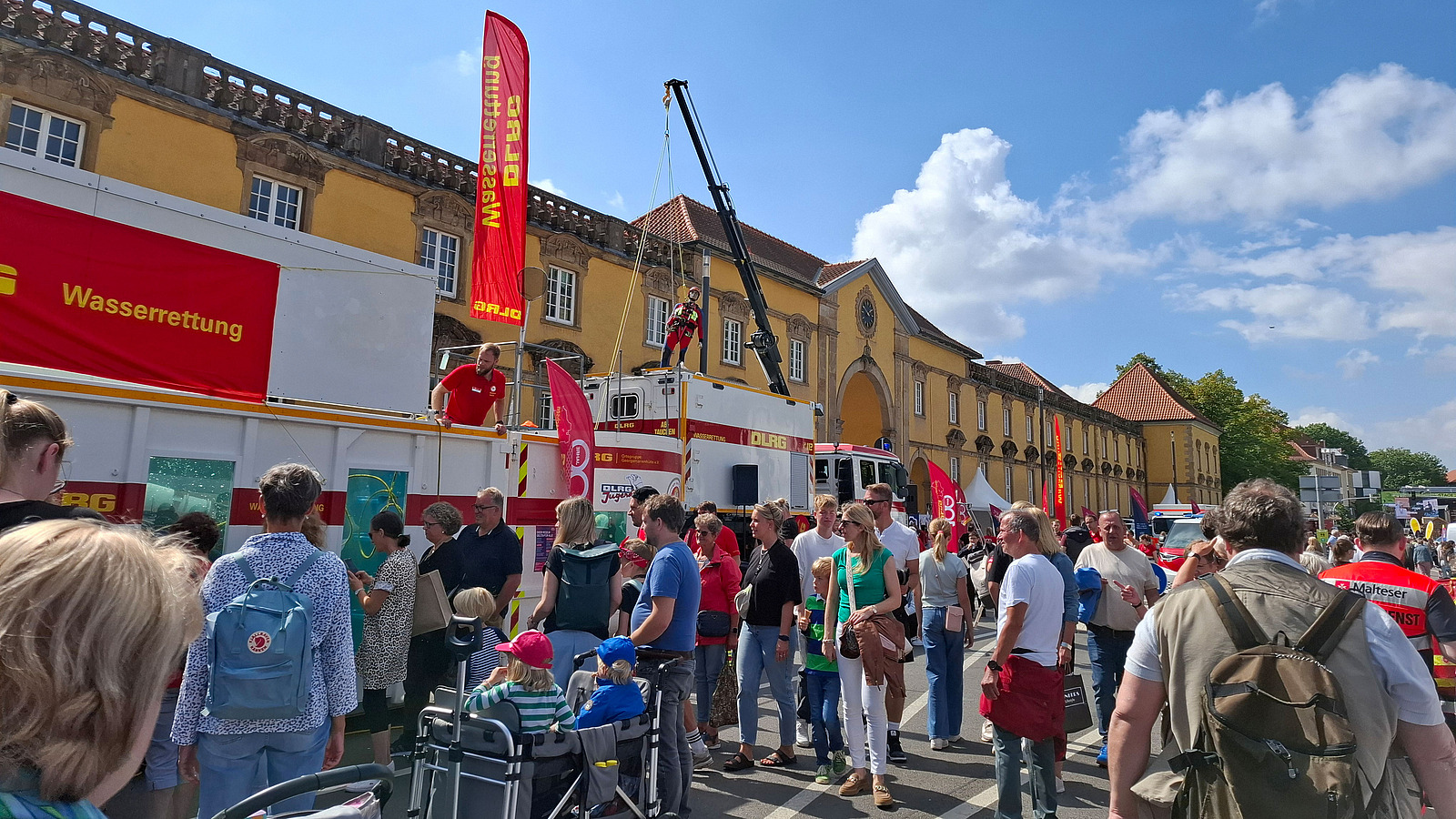Crowd around a fire truck with a lifting platform in front of a historic building.