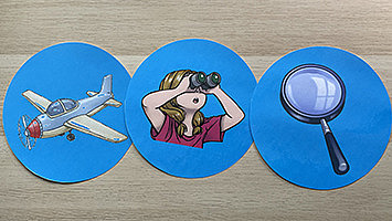 Drei blaue Deckel zeigen verschiedene Abbildungen: ein Flugzeug, eine Lupe und ein Kind, das ein Fernglas vor die Augen hält.