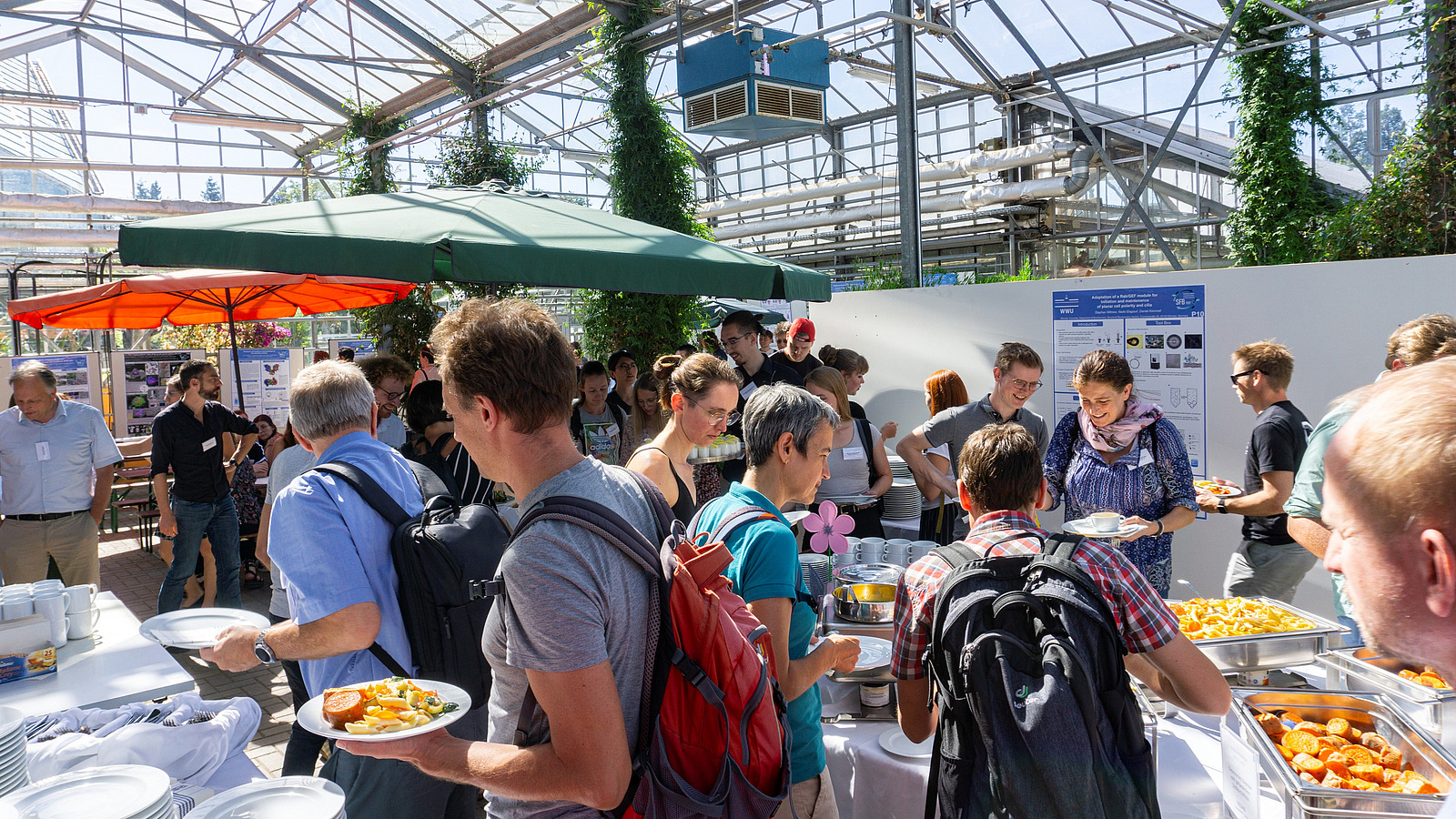 People are helping themselves to a buffet, with scientific posters visible in the background.